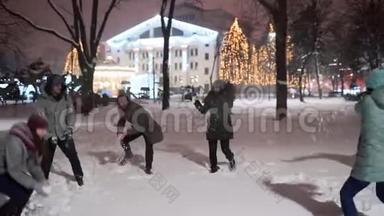 一群朋友在冬天的雪夜在城市公园玩雪球玩得很开心。 年轻的白种人喜欢下雪